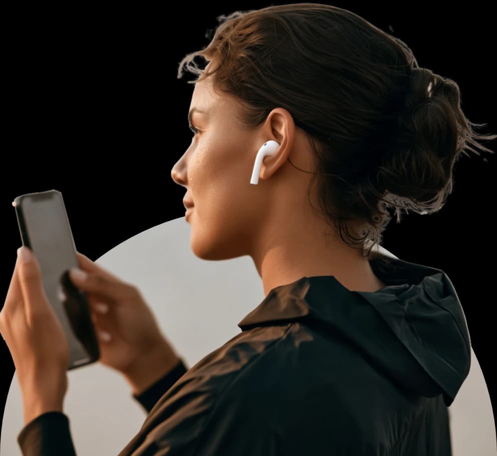 A woman listening through wireless earbuds while looking at her phone.